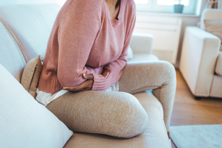 Woman holding lower abdomen while experiencing PMS cramps and menstrual pain at home.