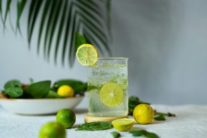 Glass of lemon water with fresh limes, lemons and leafy greens supporting natural detoxification