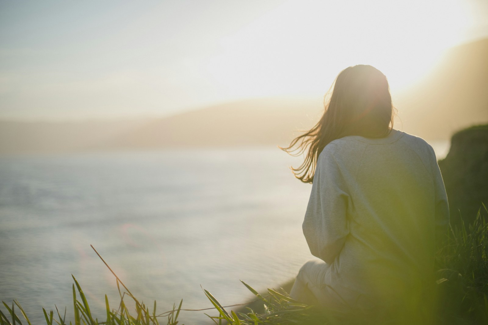 Woman sitting peacefully by the sea in soft morning light, representing balanced mood and calm